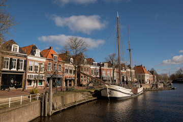 waterside residential houses and shops on the edge of the river grootdiep with ship Stichting Tromp waterway in Dokkum, Friesland, Netherlands Holland. town centre with bridge on pleasant sunny day - obrazy, fototapety, plakaty