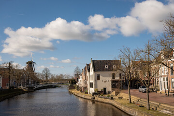 Naklejka na ściany i meble waterside residential houses on the edge of the river kleindiep waterway in Dokkum, Friesland, Netherlands Holland. windmill zeldenrust on skyline on clear sunny day