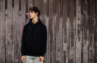 Obraz premium City portrait of handsome young guy wearing black blank hoodie or sweatshirt with space for your logo or design. Mockup for print