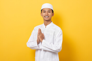 Young handsome asian muslim man gesturing greetings during ramadan isolated on orange background. happy ramadan and eid al fitr.