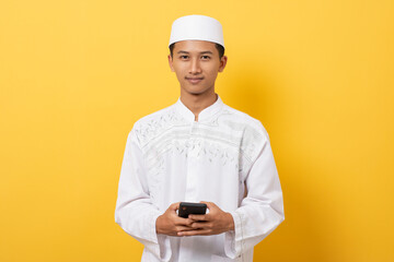 Young handsome asian muslim man smiling using smartphone standing over orange background