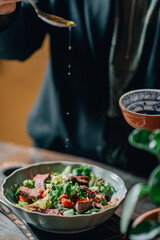 woman pouring olive oil on meat salad with herbs