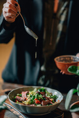 woman pouring olive oil on meat salad with herbs