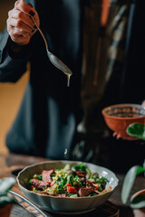 woman pouring olive oil on meat salad with herbs