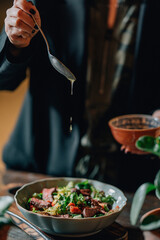 woman pouring olive oil on meat salad with herbs