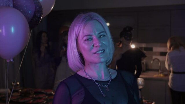 Masquerade party at home - blonde adult woman playing with red feather tickler in front of a camera