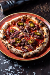pizza with meat and jalapeno peppers on black wood table