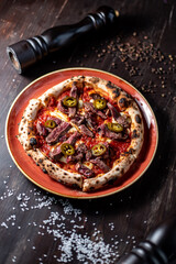 pizza with meat and jalapeno peppers on black wood table