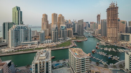 Naklejka premium Panorama showing Dubai Marina with several boat and yachts parked in harbor and skyscrapers around canal aerial timelapse.