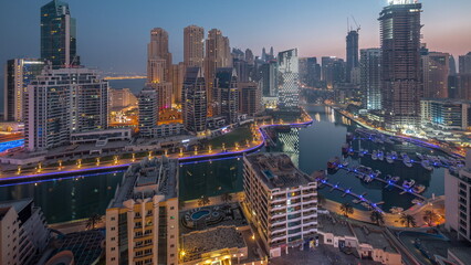 Naklejka na ściany i meble Dubai Marina with several boats and yachts parked in harbor and skyscrapers around canal aerial night to day timelapse.
