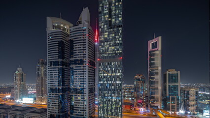 Panorama showing aerial view of Dubai International Financial District with many skyscrapers night timelapse.
