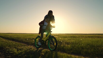 Childhood dream to ride bike. Mom teaches her little daughter to ride bicycle, sunset, Young mother...