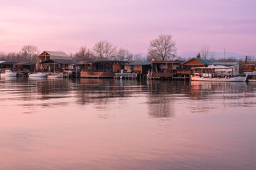Obraz premium A purple sky is reflected in the water of a river with houses and a boat in the water.