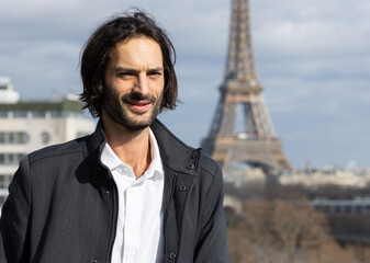 Portrait d'un beau jeune homme brun souriant avec la Tour Eiffel et Paris en arrière plan