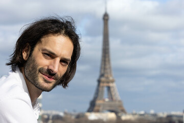 Portrait d'un beau jeune homme brun souriant avec la Tour Eiffel et Paris en arrière plan