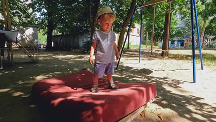 A little smiling boy jumps on a mattress in the street. Adorable preschooler having fun. Copy space - concept of play, good mood, child hyperactivity, parenting, active lifestyle, walk, dream