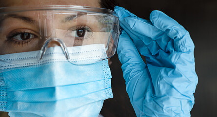 portrait of a nurse or doctor dressed in work clothes and protective accessories, wearing goggles, blue latex gloves and a surgical mask. Protection against infectious diseases.