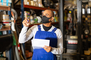 Confident hispanic worker in protective face mask taking inventory of goods in building materials...