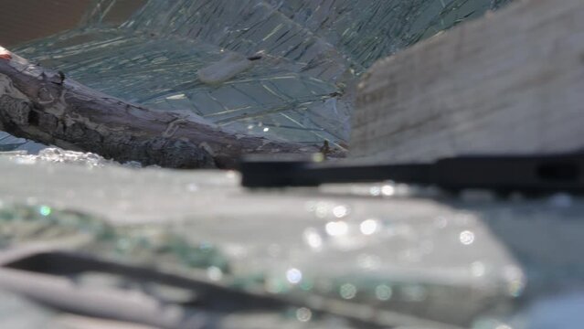 Closeup shot of the remains of a broken windshield of a car. Window broken due to vandalism. A plank was used to break into the vehicle. Camera slowly turning right.