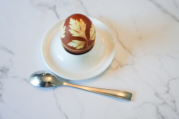 Decorated Easter egg close up on a white plate with a spoon