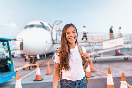 Travel woman arriving at destination coming out of plane after flight at airport. Happy young Asian tourist girl walking on outside tarmac for vacation business trip