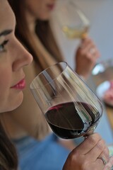 Women taste wine together, close up view with woman in blurred background, vertical format.