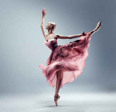 Fototapeta Ballerina in Pink Chiffon Dress jumping Split. Ballet Dancer in Silk Gown Pointe Shoes. Graceful Woman in Tutu Skirt dancing over Gray Background