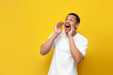 young african american guy in white t-shirt shouts loudly to the side on yellow isolated background