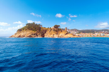 Fototapeta na wymiar View from the Mediterranean Sea of the beachfront Spanish town of Tossa de Mar, Spain, along the Costa Brava coast, with the tower of it's medieval castle and beach in view.