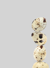 Stacked speckled quail eggs on light grey background. Space for text