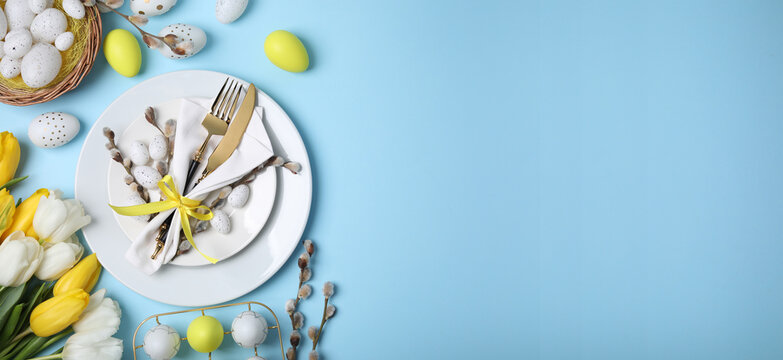 Festive Easter table setting with tulips and painted eggs on light blue background, flat lay. Banner design with space for text