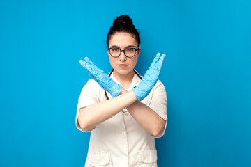 doctor woman in uniform shows stop gesture with hand on blue background, nurse in medical gown shows refusal symbol