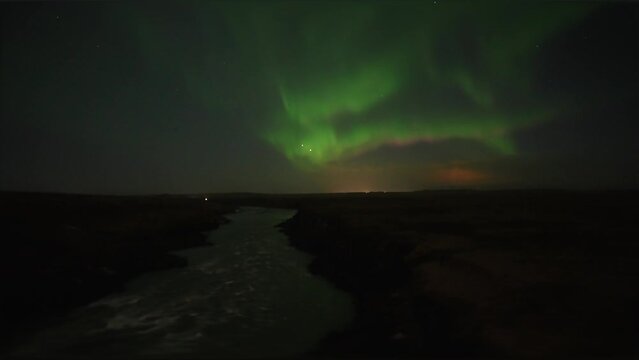 Wide shot of Aurora Borealis at night sky and flowing river in darkness on Iceland