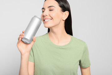 Beautiful happy woman drinking from beverage can on light grey background