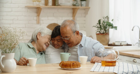 Asian senior couple kindly embracing their teen granddaughter at kitchen table, enjoying their togetherness - family times, relationship, love concept 