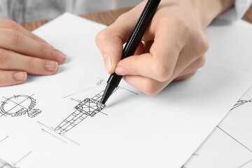 Jeweler drawing sketch of elegant ring on paper at wooden table, closeup