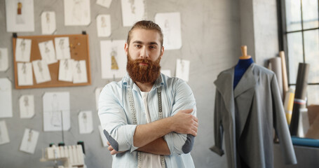 Fototapeta premium A hipster clothing designer working in his loft office, creating a new clothes collection, looking at camera and smiling - fashion, small business concept 