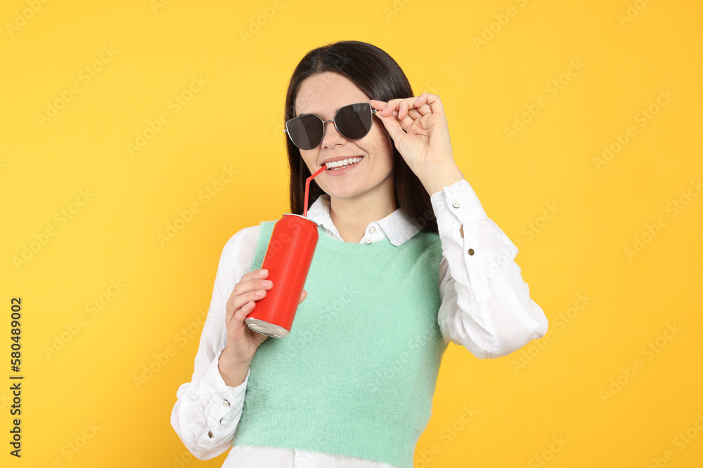 Poster Beautiful happy woman drinking from red beverage can on yellow background