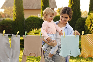 Mother and daughter hanging clothes with clothespins on washing line for drying in backyard