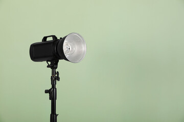 Studio flash light with reflector against pale green background, space for text. Professional photographer's equipment