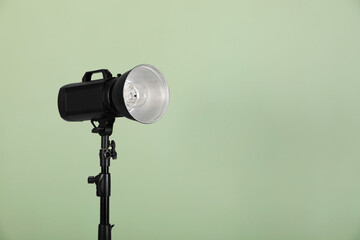 Studio flash light with reflector against pale green background, space for text. Professional...