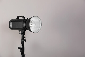 Professional studio flash light with reflector on tripod against grey background, space for text. Photography equipment