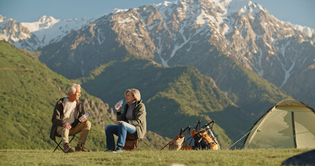 Fototapeta premium Old couple, Retired Persons. elderly couple sits on top of a mountain near a tent and talks at sunset. 