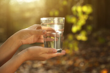 Woman holding glass of fresh water in forest, closeup