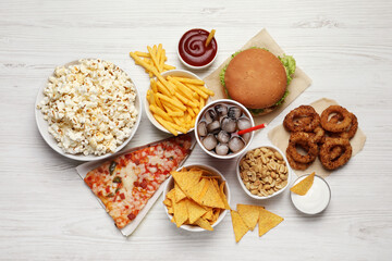 French fries, pizza and other fast food on white wooden table, flat lay