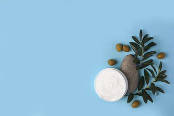 Flat lay composition with jar of cream and olives on light blue background. Space for text