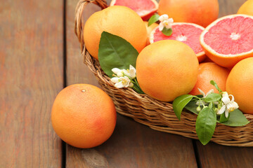 Wicker basket with fresh grapefruits and green leaves on wooden table
