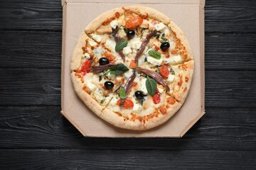 Tasty pizza with anchovies, basil and olives on black wooden table, top view
