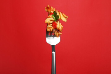 Fork with tasty pasta on red background