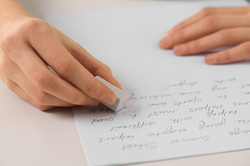 Fototapeta na wymiar Girl erasing mistake in her notebook at white desk, closeup